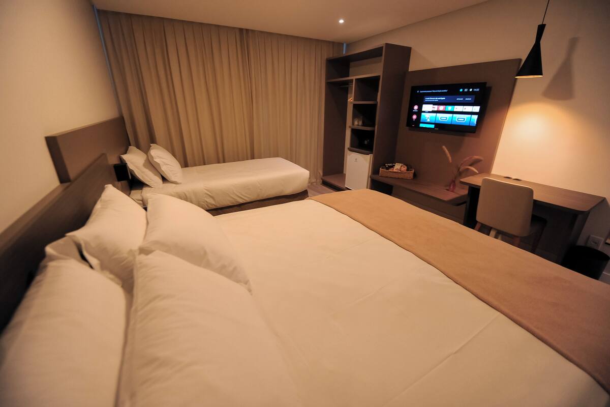 Habitación de hotel con dos camas, un televisor montado en la pared, un escritorio con una silla y un armario.