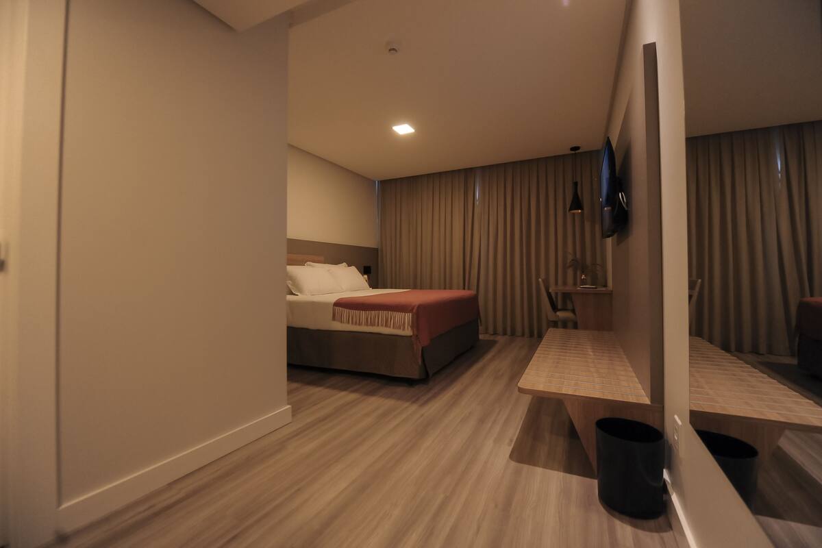 Una habitación de hotel con cama, televisor, una mesita y un espejo.