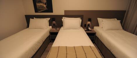 A hotel room with two single beds, a large bed, and a headboard with a picture.