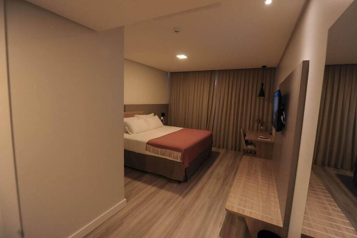 Una habitación de hotel con una cama, un escritorio, una silla, un televisor y una cortina.