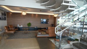 A modern living room with a sofa, chairs, a coffee table, and a TV. There is a staircase with glass railings and a potted plant. - Figueiras Hotel & Eventos (Sao Miguel Do Oeste)