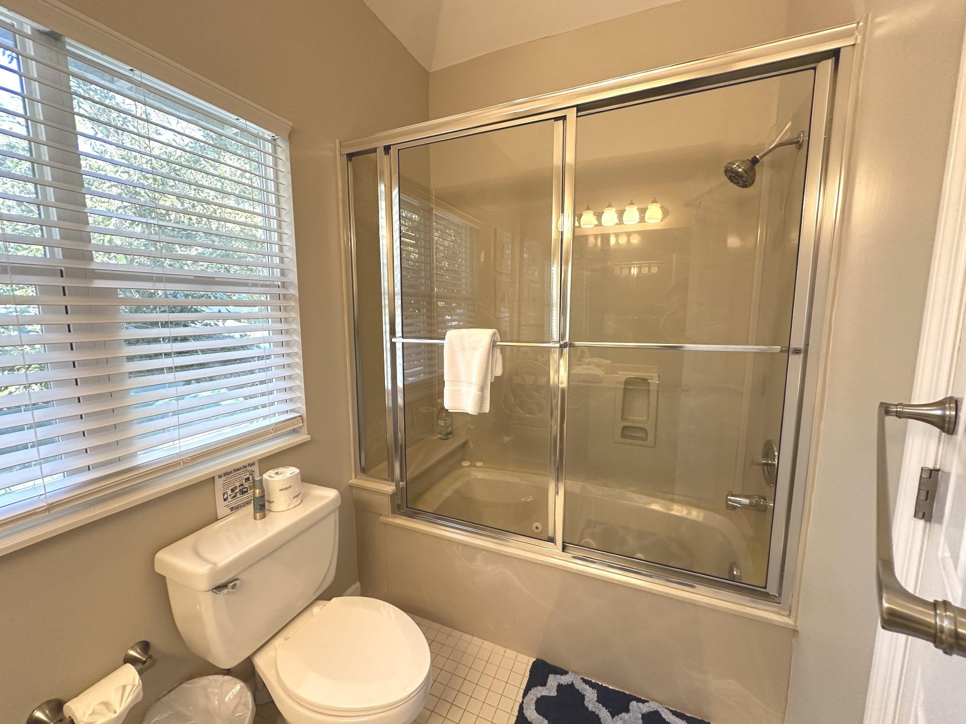 Une salle de bain avec une douche à parois de verre, des toilettes et une fenêtre équipée de stores.