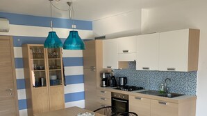 A modern kitchen with a dining area, featuring a striped wall, blue pendant lights, and a tiled backsplash. - Pool apartment in quiet and central area (Colico , Lombardei)
