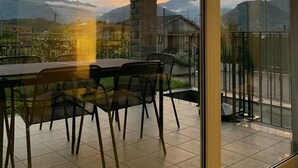 A balcony with a table and chairs, overlooking a mountainous landscape with a sunset. - Pool apartment in quiet and central area (Colico , Lombardei)