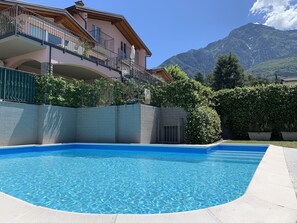 A swimming pool with a mountain backdrop, a multi-story building with balconies, and a clear sky.