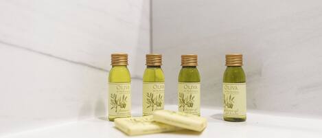 Four bottles of olive shower gel and two bars of soap on a white surface.