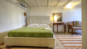 Ein ordentlich eingerichtetes Schlafzimmer mit einem Bett, einem Sessel, einem Schreibtisch und einem Bild an der Wand.
