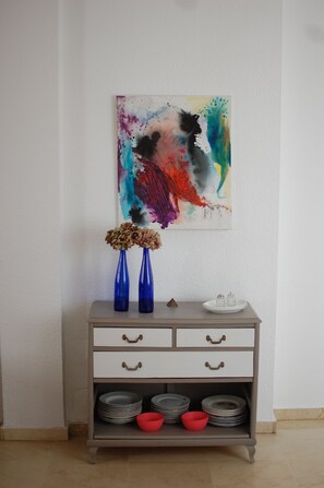 Une commode grise, surmontée d’une peinture abstraite aux couleurs vives, et agrémentée de deux vases bleus.