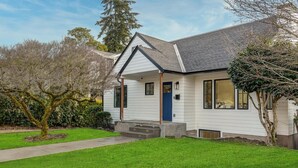 Ein zweistöckiges Haus mit Veranda, blauer Tür und gepflegtem Rasen.