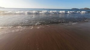 A beach with waves gently lapping onto the shore under a clear sky. - Villas El Ron Ron (Cartagena)