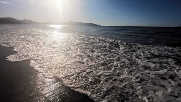 A beach with waves and a distant mountain range under a clear sky. - Villas El Ron Ron (Cartagena)