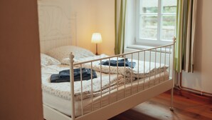 Un llit individual amb estructura metàl·lica, una làmpada de nit i una finestra amb cortines.