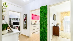 Un intérieur moderne avec un mur blanc, un jardin vertical verdoyant, une cuisine aux armoires roses et un téléviseur fixé au mur.