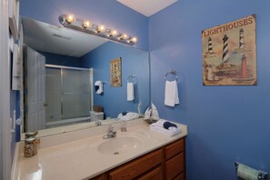 A bathroom with a large mirror, a sink, and a towel rack. There is a poster on the wall and a light fixture above the mirror. - Close to PF Parkway, spacious & clean 3 bedroom! Hot tub and outdoor TV on deck! (PIGEON FORGE)