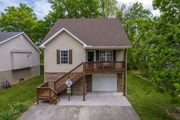 A two-story house with a front porch, a garage, and a small front yard. - Close to PF Parkway, spacious & clean 3 bedroom! Hot tub and outdoor TV on deck! (PIGEON FORGE)