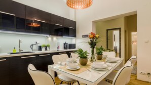 Una cocina moderna con armarios oscuros, una mesa de comedor de vidrio, sillas blancas y una lámpara colgante.