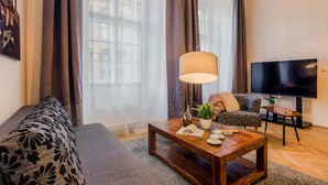 Una sala de estar con un sofá, una mesa de centro con objetos decorativos, un televisor y una ventana con cortinas.