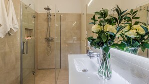 Un baño moderno con ducha de vidrio, un lavamanos blanco y un jarrón con flores.