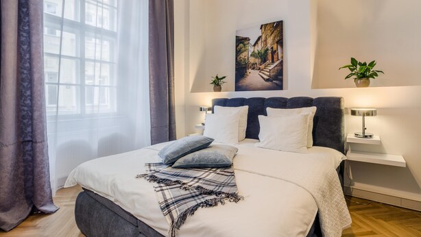 Un dormitorio moderno con una cama grande, un cabecero, dos mesitas de noche, una lámpara colgante y una ventana con cortinas.