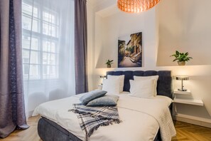 Ein modernes Schlafzimmer mit einem großen Bett, einem Kopfteil, zwei Nachttischen, einer Pendelleuchte und einem Fenster mit Vorhängen.