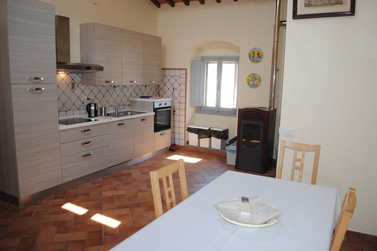 A kitchen with wooden cabinets, a tiled backsplash, a window with shutters, and a dining table with chairs.