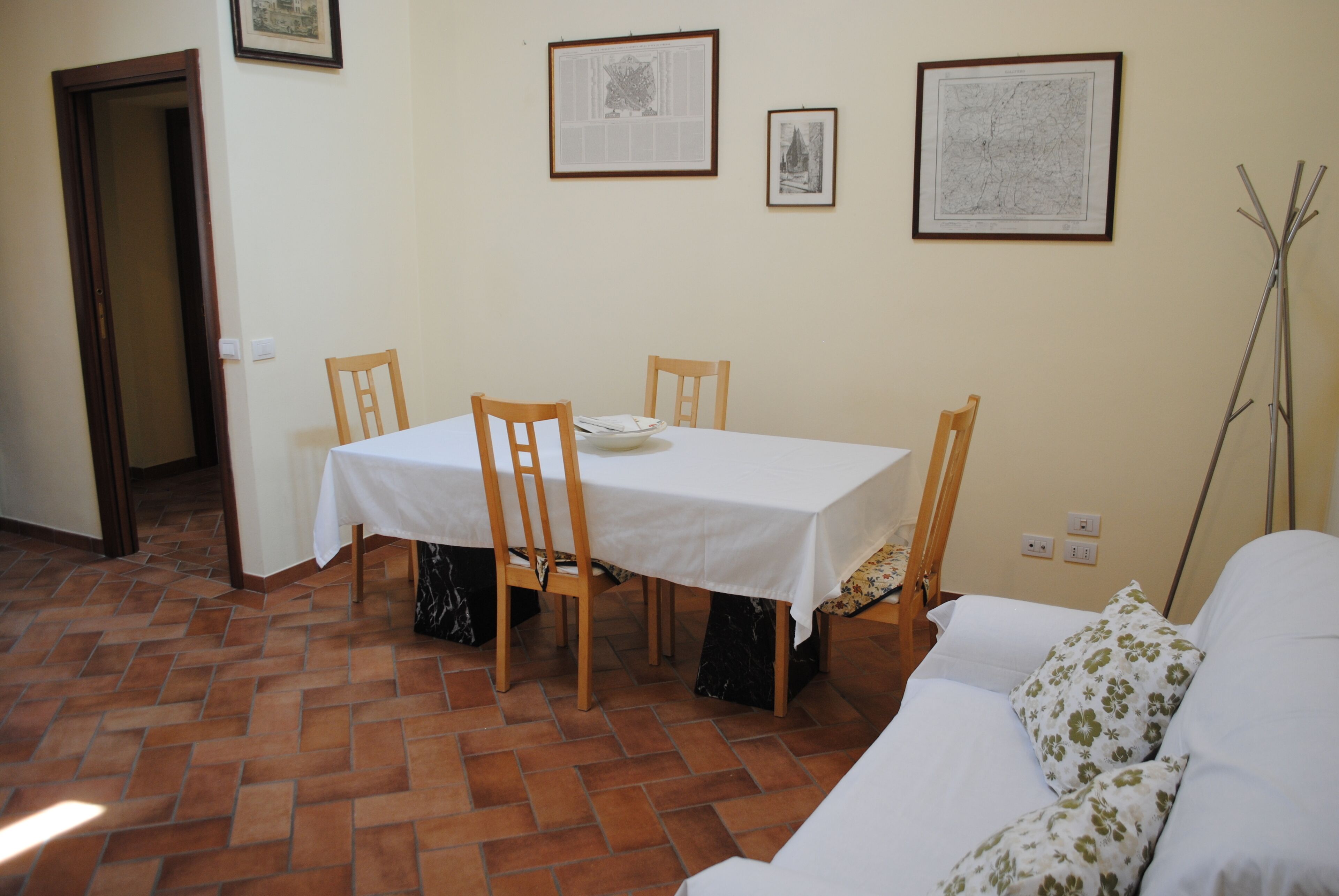 Un coin repas avec une table, des chaises et une nappe blanche. Des tableaux encadrés ornent le mur, et un porte-manteau se trouve à droite.