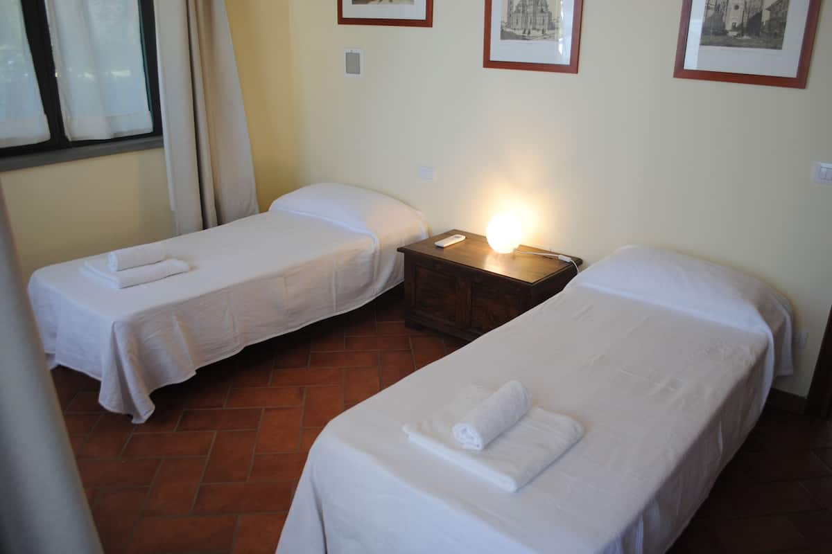 A hotel room with two single beds, a nightstand with a lamp, and a window with curtains.