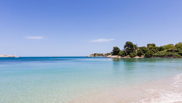 A beach with clear turquoise water, a sandy shore, and a small island with trees and buildings.