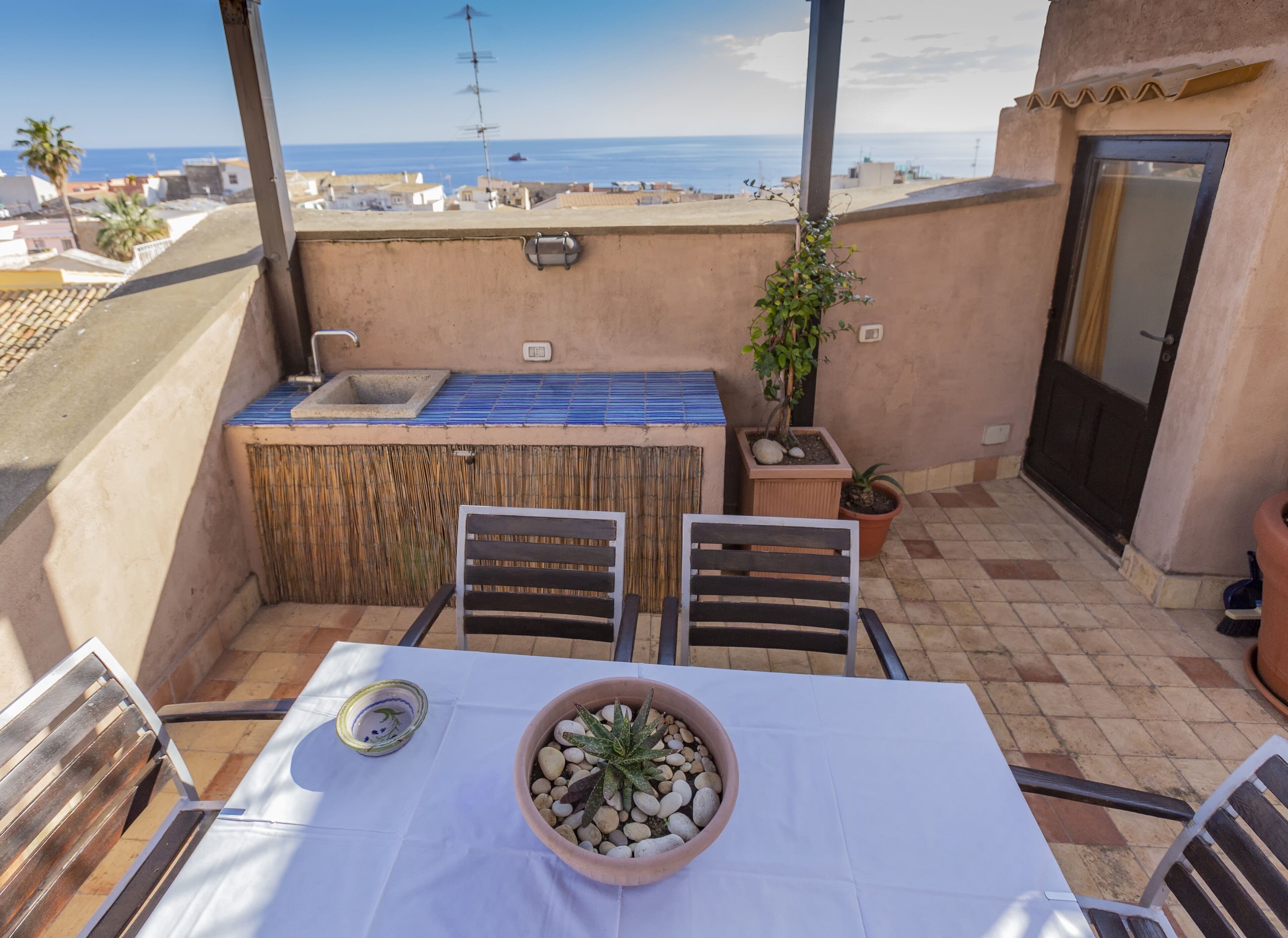 A small outdoor patio with a table, chairs, a small bar area, and a view of the sea.