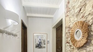 A hallway with a framed poster, a wooden bench, a patterned rug, and a stone wall.