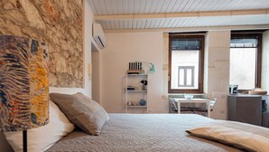 A bedroom with a bed, a desk, a chair, a shelf with books and a lamp, and a window.