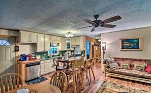 A spacious kitchen with wooden cabinets, a dining area with a table and chairs, a sofa with patterned cushions, and a ceiling fan.