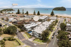 An aerial view of a residential area with modern buildings, a beach, and a Leisure Island. - Sunny & Spacious, Downtown Mount, Beach & Pool (Mount Maunganui)