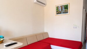 A room with a beige sofa, a red blanket, a remote control, and a framed picture of a waterfall on the wall. - Apartment 30 metres from the beach (Sainte-Luce)