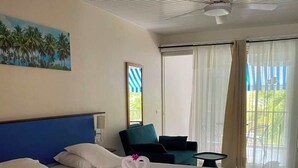 A hotel room with a bed, a ceiling fan, a painting, a chair, and a view through the window. - Apartment 30 metres from the beach (Sainte-Luce)