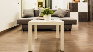 A modern living room with a grey sofa, a white coffee table with a plant, and a wooden floor.