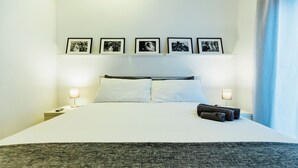 A hotel room with a large bed, two bedside tables, a flat-screen TV, and a wall-mounted picture frame with four photos.