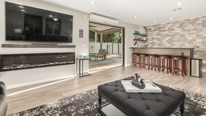 Ein modernes Wohnzimmer mit Kamin, Fernseher und Küchenzeile mit Barhocker.