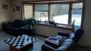A living room with a large window, a black and white checkered coffee table, a brown leather sofa, and a small wooden table with a plant.