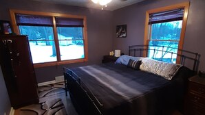 A bedroom with a bed, a ceiling fan, two windows, a dresser, and a patterned rug.