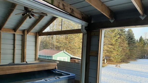 A cabin with a hot tub, a wooden deck, and a view of a snowy landscape.