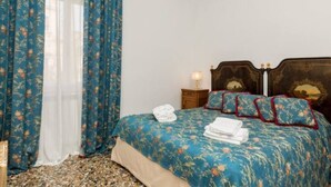 Une chambre à coucher avec une couvre-lit à motifs floraux, une tête de lit en bois et une table de chevet avec une lampe.