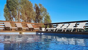 Una piscina con agua cristalina azul, rodeada de sillones blancos y una terraza de madera.