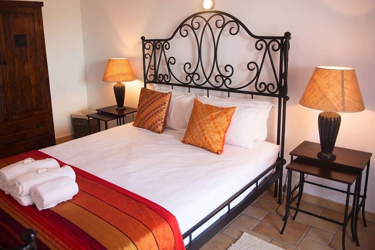 Een opgemaakt bed met een rood-wit gestreept dekbed, twee kussens, twee nachtkastjes met lampen en een houten garderobe.