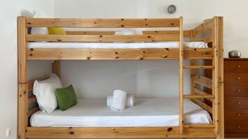 Una cama litera con estructura de madera, ropa de cama blanca y almohada verde.