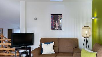 Una sala de estar con un sofá, televisor, una mesa de centro y una lámpara de pie.