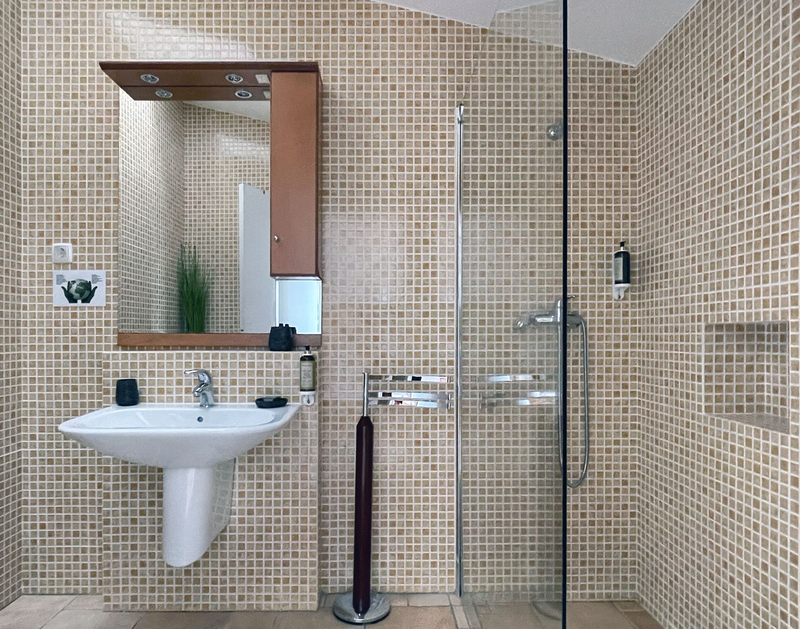 Un baño con lavamanos blanco, espejo y ducha con mampara de vidrio.