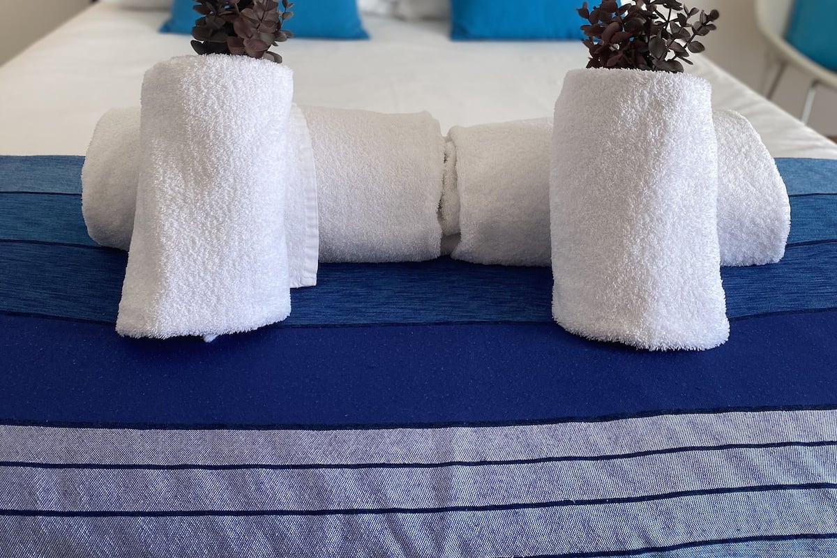 Een netjes opgemaakt bed met blauwe en witte kussens, twee witte handdoeken en decoratieve planten, en een blauw sprei.
