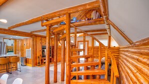 A log cabin interior with a wooden staircase, a dining area with chairs, and a kitchen visible through an open door. - 6Bdrm Cabin Walk to Beach Pool-Table Firepit! (Kingston)