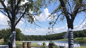 Een pad van stenen dat leidt naar een gelegenheid aan het meer, met witte tafels en stoelen, omgeven door grote bomen.